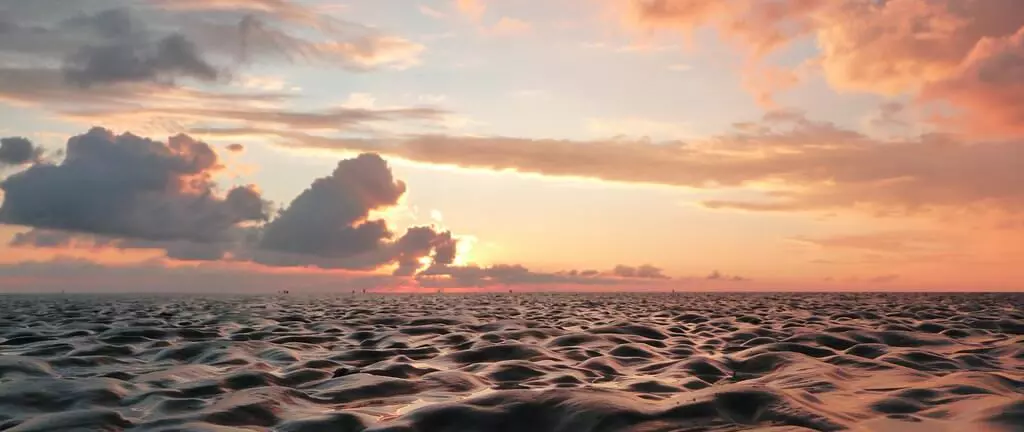 Wattenmeer bei Sonnenuntergang mit spiegelndem Wasser und buntem Himmel voller Wolken am Horizont