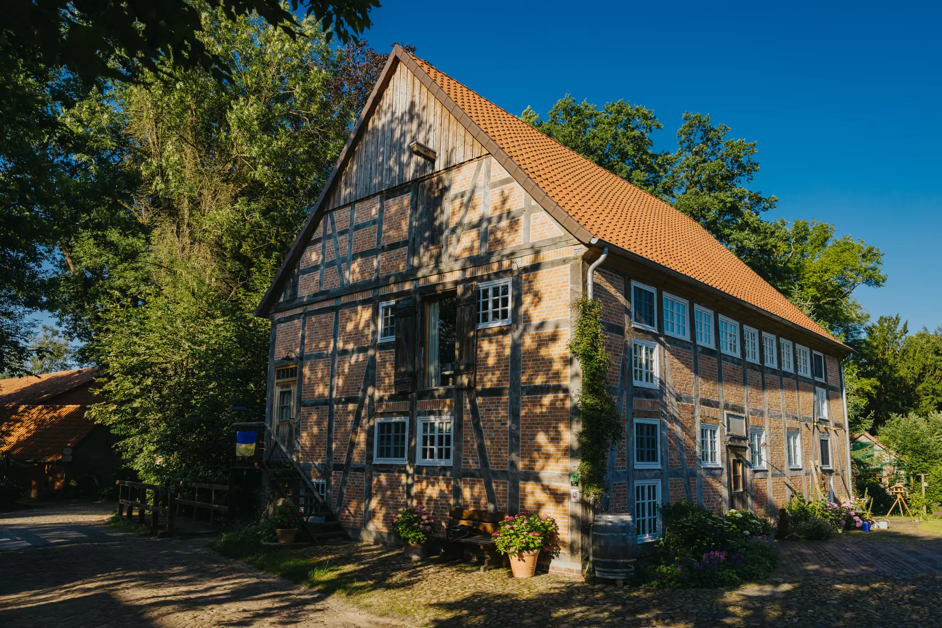 Fachwerkhaus mit rotem Ziegeldach und blauen Fensterrahmen in Worpswede, umgeben von Bäumen und sommerlichem Grün unter blauem Himmel