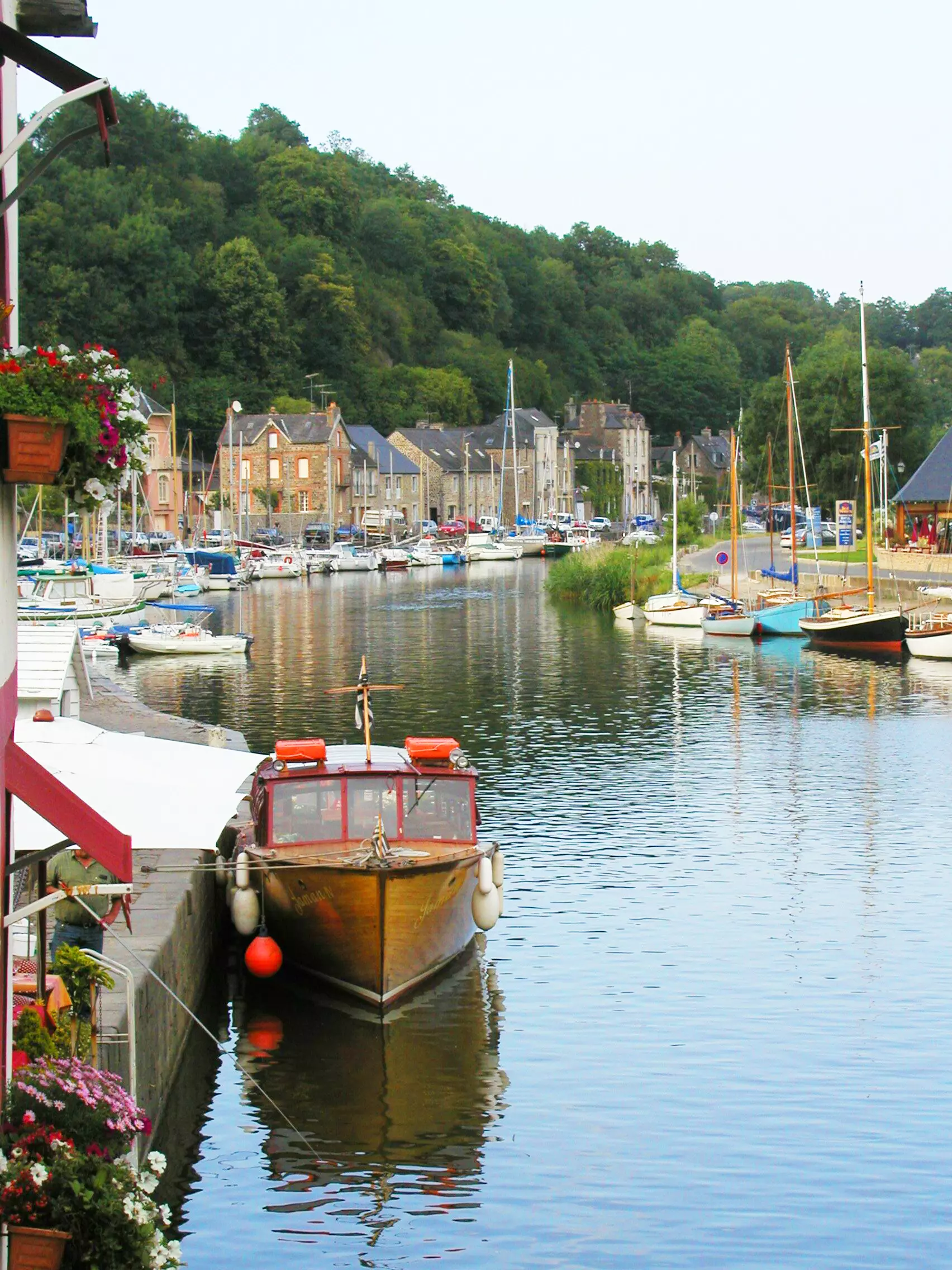 Hafen in Cancale mit Segel- und Motorbooten, Häusern am Ufer und bewaldeten Hügeln im Hintergrund