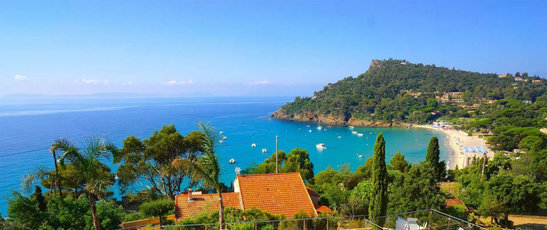 Malerische Küstenlandschaft in Frankreich mit blauem Meer, Sandstrand, Segelbooten und bewaldetem Hügel im Hintergrund