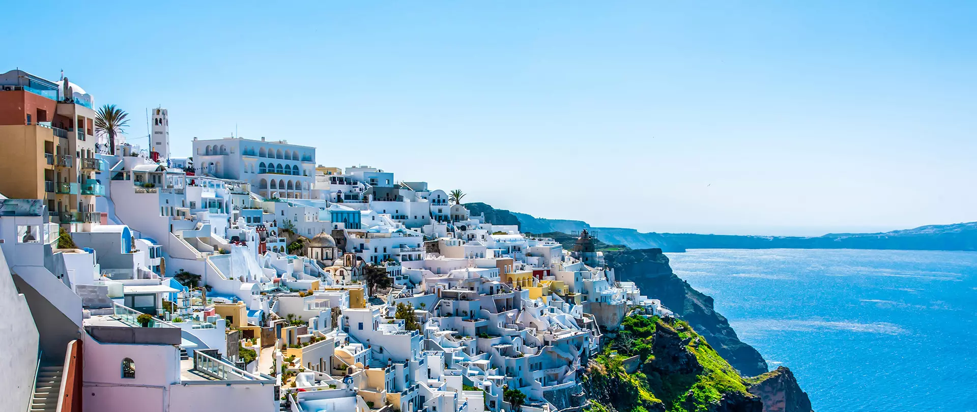 Weiße Häuser und Hotels an einer steilen Küste mit Blick auf das blaue Meer bei klarem Himmel auf Santorin
