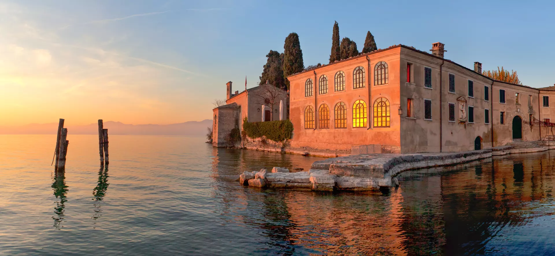 Sonnenuntergang über historischen Gebäuden am Ufer des Gardasees mit ruhigem Wasser und sanfter Abendstimmung