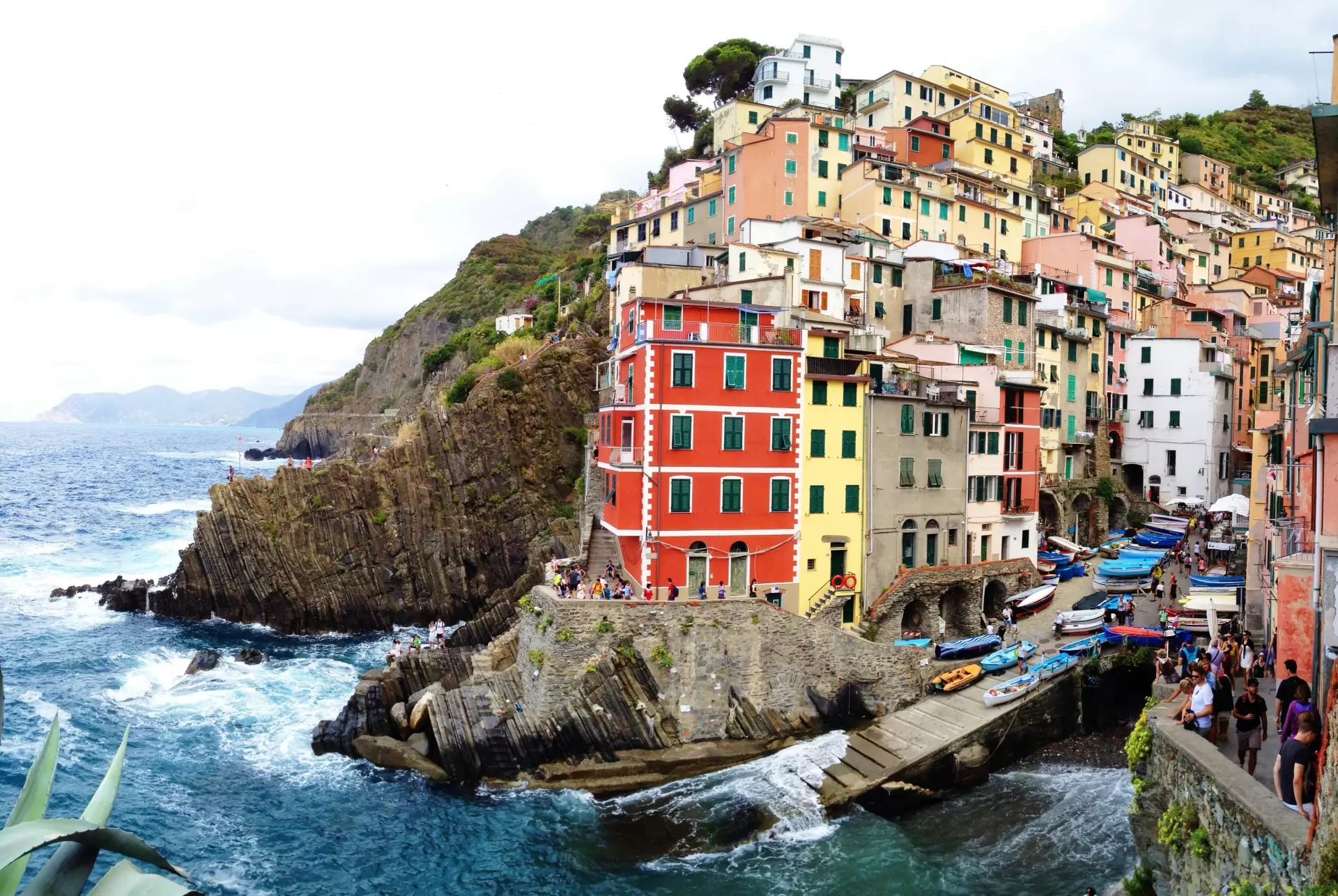 Bunte Häuser an steiler Küste über dem Meer in der typisch ligurischen Küstenstadt Riomaggiore, mit Booten und Felsen im Vordergrund