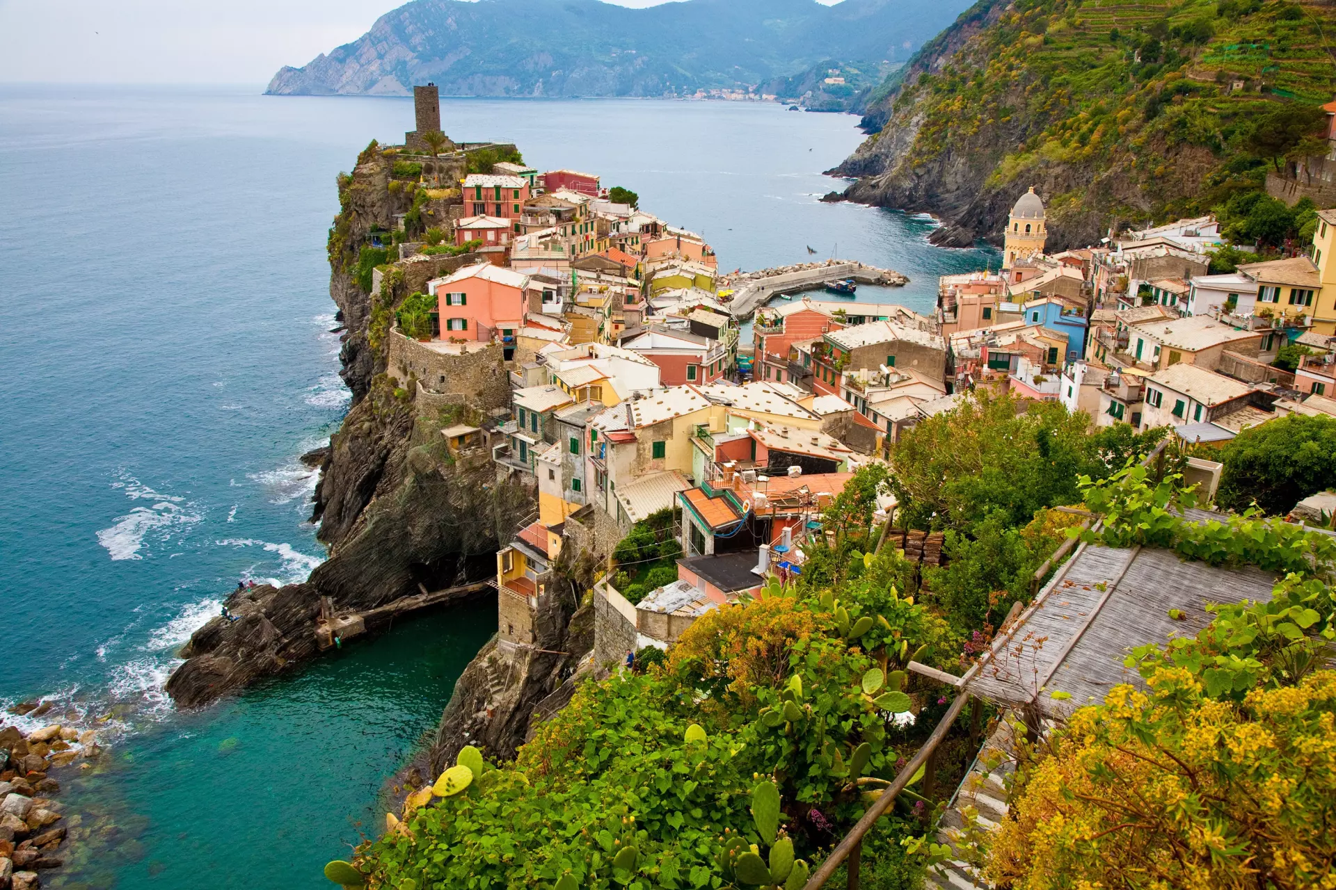 Bunte Häuser auf steilen Klippen entlang der ligurischen Küste mit Blick auf das Meer und bewachsene Hänge im Vordergrund