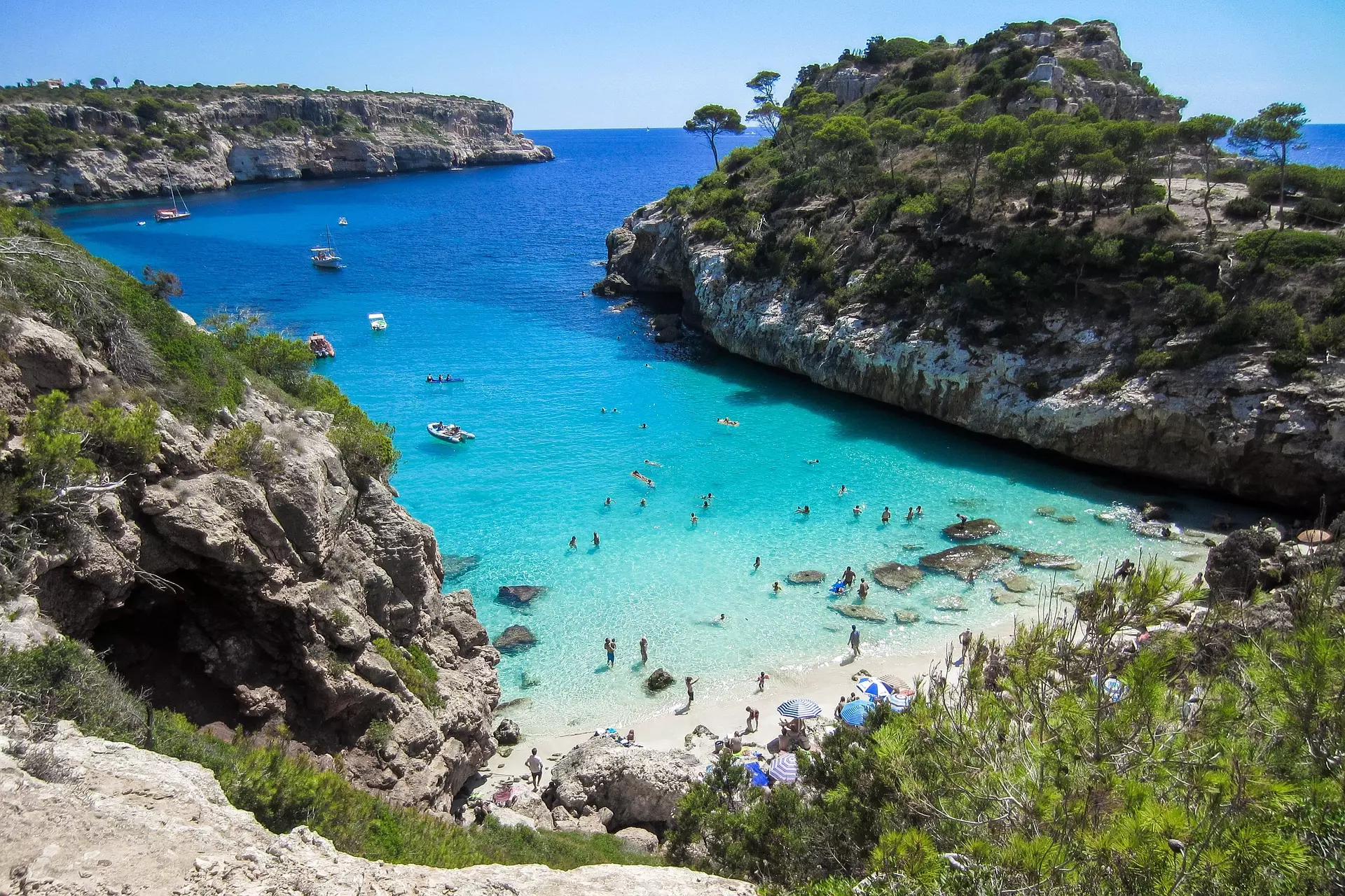 Kleine Bucht mit klarem türkisfarbenem Wasser, Felsenklippen und Menschen am Strand und im Wasser auf Mallorca