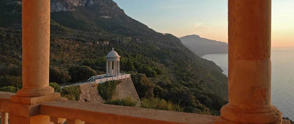 Tempel auf einem Hügel mit Blick auf Meer und Berge bei Sonnenuntergang, aufgenommen von einer Terrasse mit Säulen in Mallorca