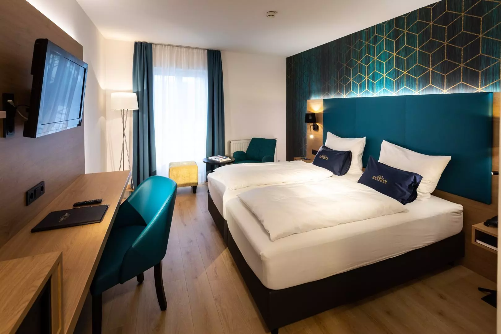 Modern eingerichtetes Hotelzimmer im Hotel Messmer in Bregenz mit Doppelbett, Schreibtisch, Fernseher und Sitzbereich vor Fenster mit Vorhängen