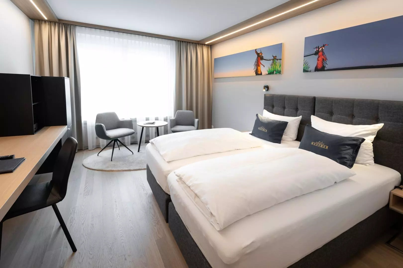 Modernes Hotelzimmer im Hotel Messmer Bregenz mit Doppelbett, Sitzbereich, Schreibtisch und zeitgenössischer Wandkunst über dem Bett