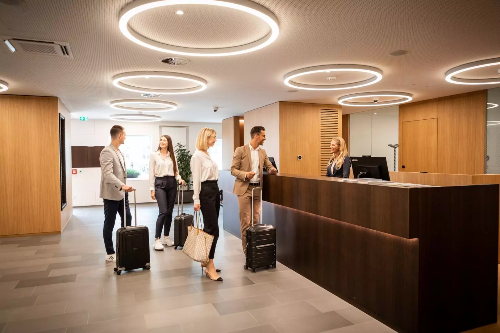 Hotelgäste mit Gepäck checken an der Rezeption des modernen Hotel Messmer in Bregenz ein, mit hellen Deckenringen und Holzvertäfelung