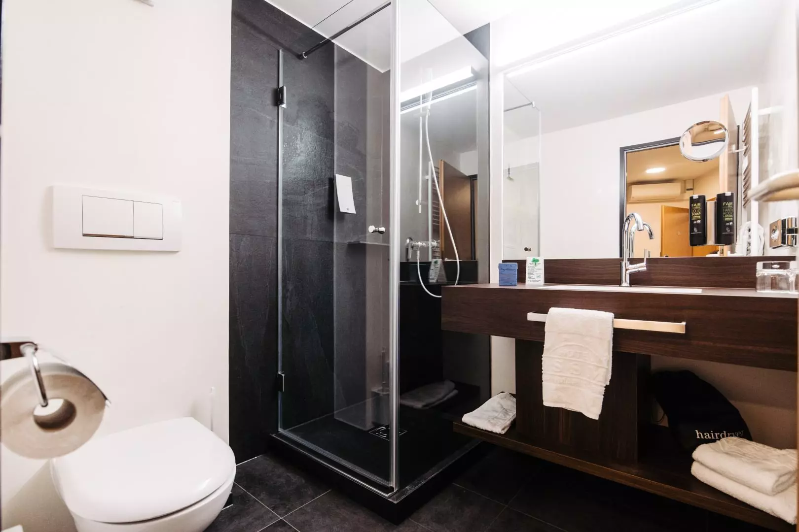 Moderne Badezimmer im Hotel Messmer Bregenz mit Dusche, WC, großem Spiegel und Holzwaschtisch mit Handtüchern