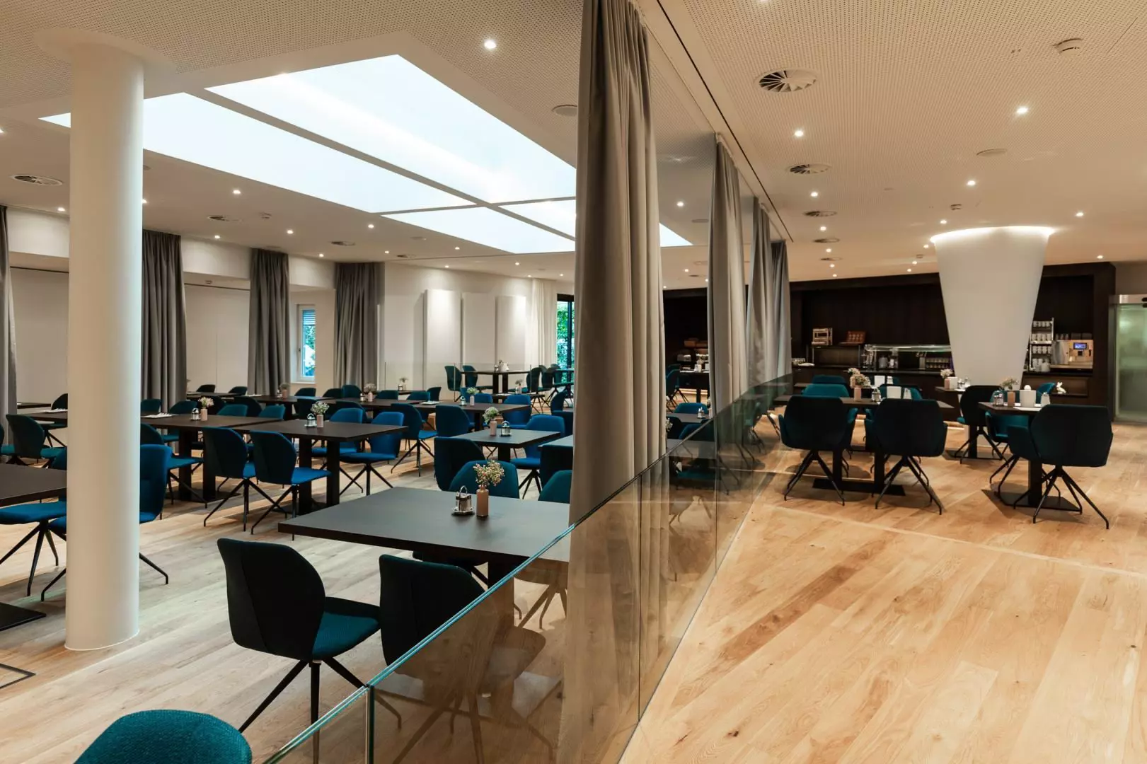 Moderne Hotel-Lounge im Hotel Messmer Bregenz mit blauen Sesseln, Holzboden, Glaswand und großem Deckenlicht