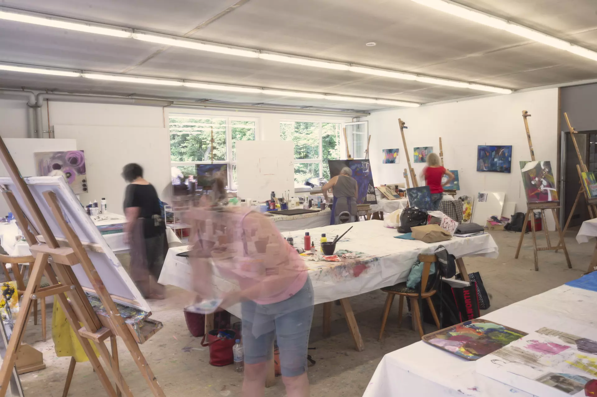 Künstlerinnen bei der Arbeit in einem hellen Atelier mit Staffeleien und Bildern in der Kunstakademie Allgäu