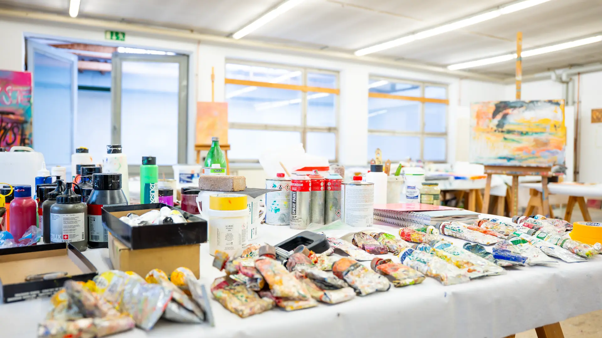 Kunstakademie Allgäu Farben und Malutensilien wie Tuben, Dosen und Pinsel auf einem Tisch im hellen Atelier der Kunstakademie Allgäu im Allgäu