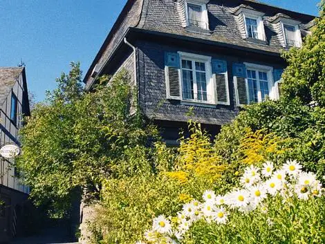 Traditionelles Landhaus mit Schieferfassade und Fensterläden, umgeben von bunten Blumen und grünem Pflanzenbewuchs in der Moselregion
