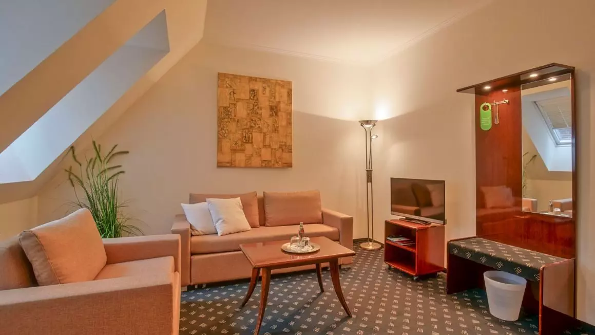 Gemütlicher Hotelzimmer-Wohnbereich mit Sofa, Sessel, TV, Spiegelkommode und Stehlampe im Hotel Worpsweder Tor in Worpswede