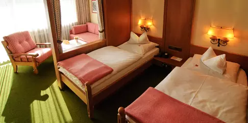 Zweibettzimmer im Steinbach-Hotel Berchtesgadener Land mit Holzmöbeln, grütem Teppich, Sofa und warmem Licht an den Wänden