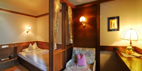 Gemütliches Hotelzimmer im Steinbach-Hotel Berchtesgadener Land mit Einzelbett, Blumenstuhl und warmer Beleuchtung