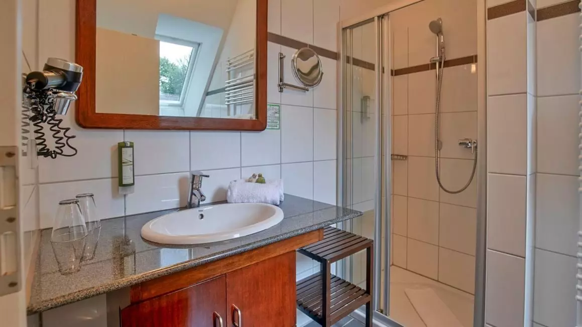 Modernes Hotelbad mit Waschbecken, Spiegel, Haartrockner und gläserner Dusche im Hotel Worpsweder Tor in Worpswede