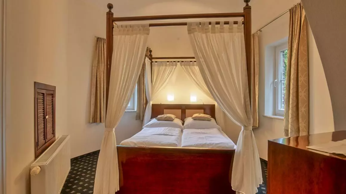 Doppelbett mit Baldachin und weißen Vorhängen in einem gemütlichen Hotelzimmer des Hotel Worpsweder Tor in Worpswede