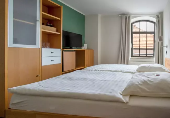 Modernes Hotelzimmer mit Doppelbett, Fernseher und großem Fenster im Hotel Birschel-Mühle in Hattingen