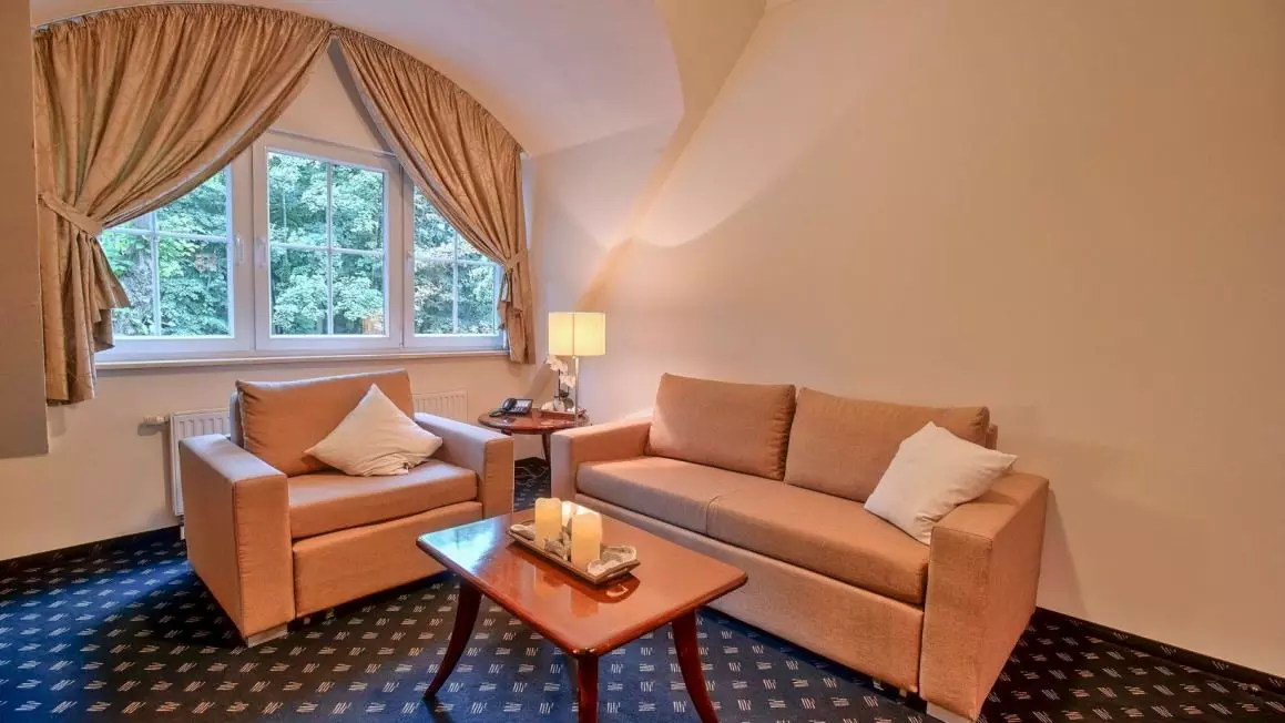 Gemütliche Sitzecke mit zwei beigen Sofas, Holztisch und Fenster mit Vorhängen in einem Hotelzimmer des Hotel Worpsweder Tor in Worpswede