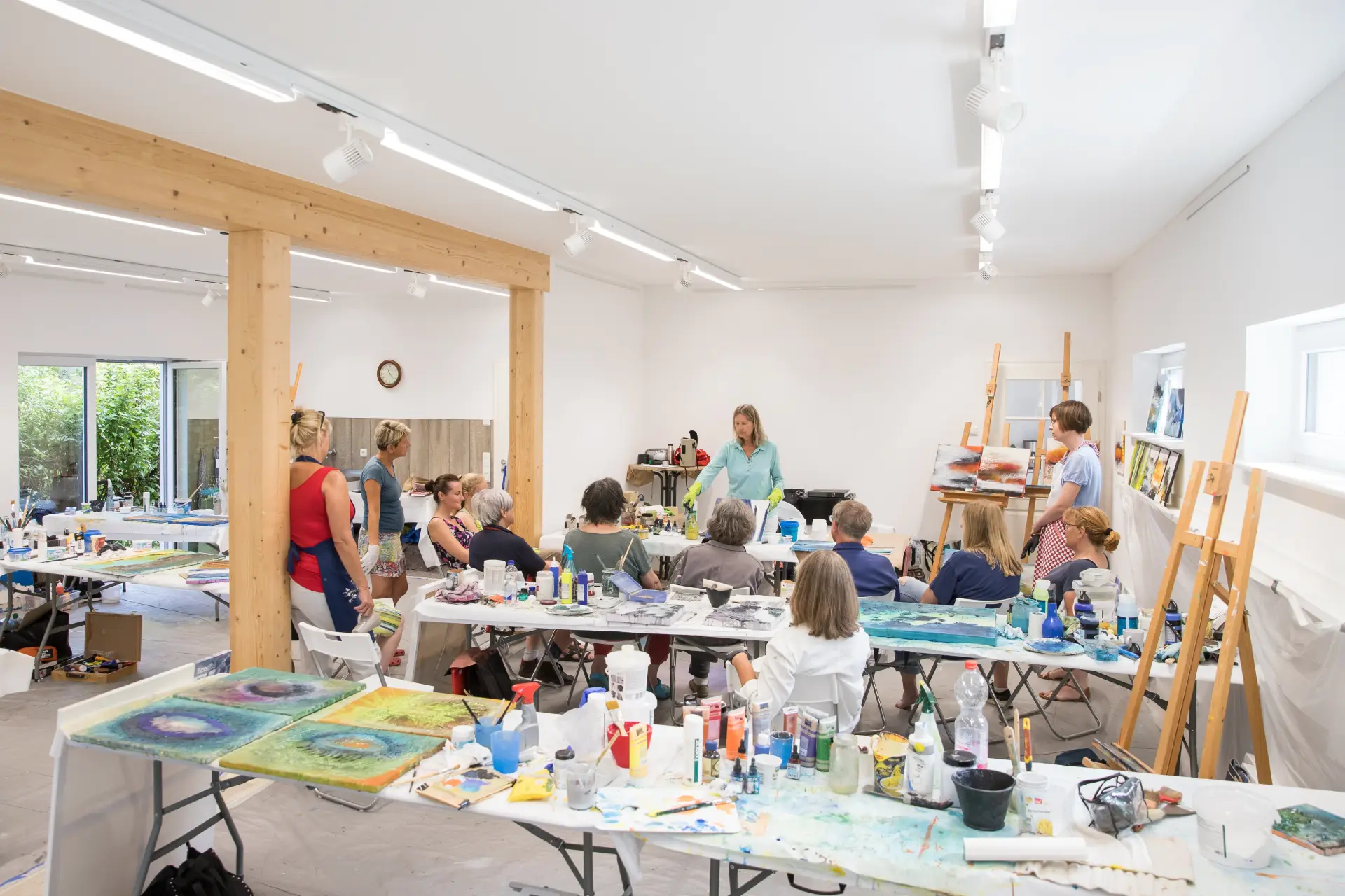 Malkurs im Künstlerhaus Prerow mit Teilnehmern an Tischen und Lehrerin im hellen Atelier mit Staffeleien und Kunstmaterialien