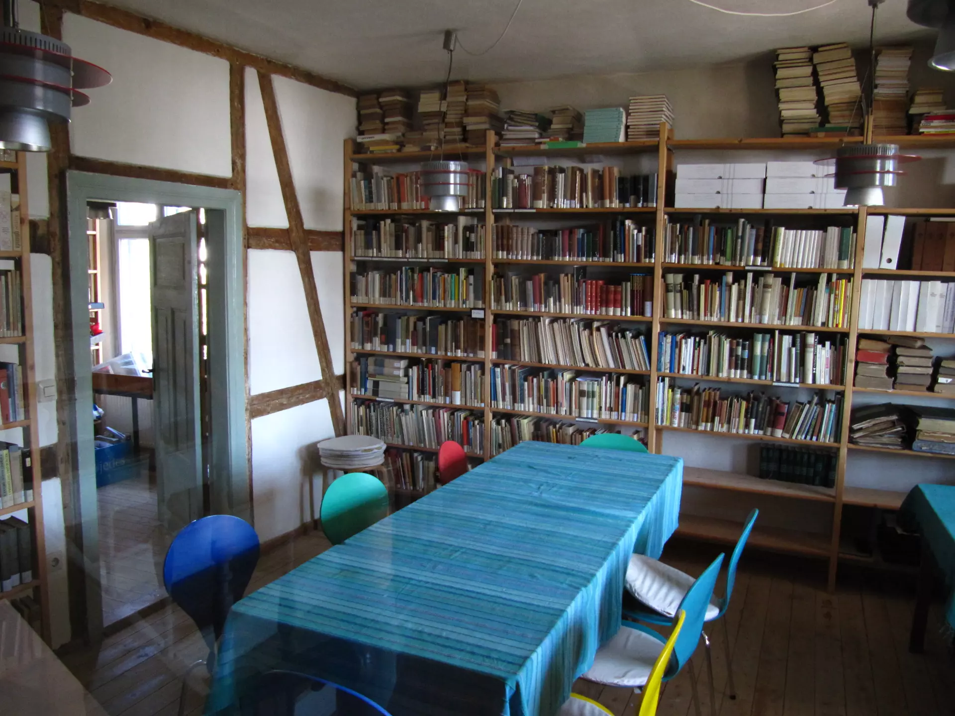 Atelier Grundvigthhaus Ruegen 2009 Sebastian(18) Atelierraum im Grundtvighaus auf Rügen mit Bücherregalen, einem Tisch mit blauem Tischläufer und bunten Stühlen