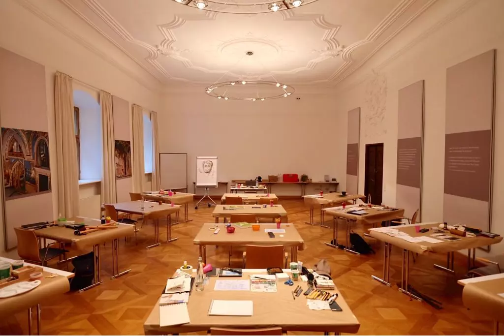Atelier Kloster Seeon Atelierraum im Hotel im Chiemgau mit mehreren Tischen, Malutensilien und einer Staffelei in hellem, kunstvoll gestalteten Raum