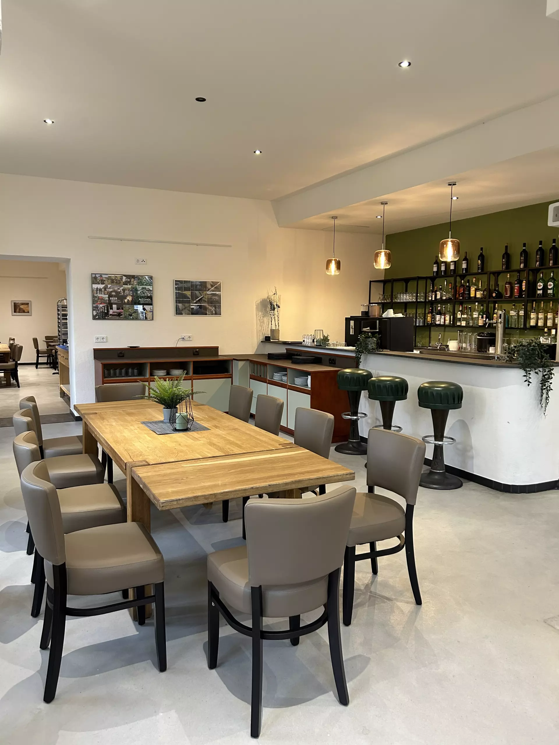 Essbereich mit Holztisch, beigen Stühlen und Bar mit grünen Hockern im Hotel Birschel-Mühle in Hattingen