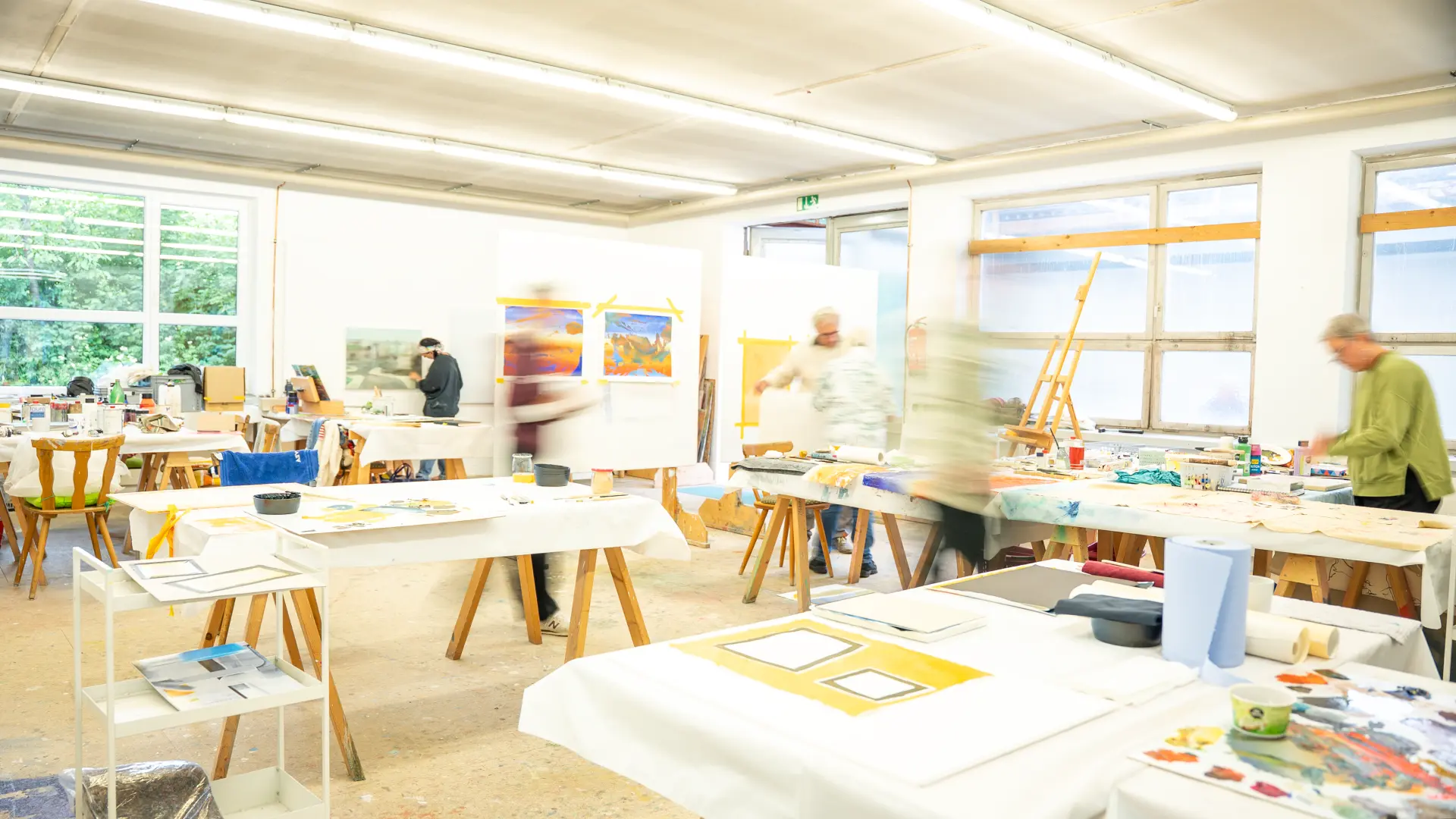 Kunstakademie Allgäu Hell erleuchtetes Atelier der Kunstakademie Allgäu mit mehreren Personen beim Malen an großen Arbeitstischen und Staffeleien
