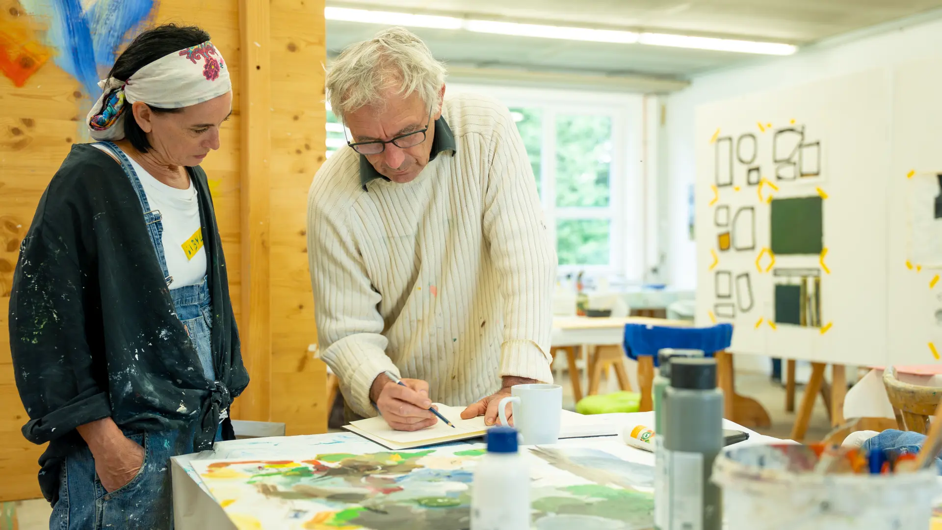Malkurs in der Kunstakademie Allgäu Zwei Künstler im Atelier der Kunstakademie Allgäu arbeiten gemeinsam an einem Gemälde auf einem Tisch voller Malutensilien