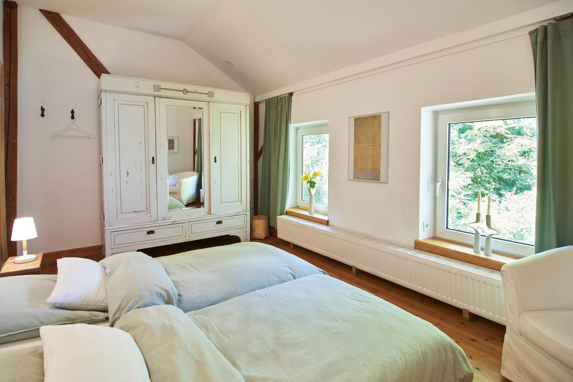 Schlafzimmer Werkgut Helles Schlafzimmer mit zwei Betten, weißem Schrank mit Spiegel, großen Fenstern und grünem Blick im Werkgut im Naturpark Aukrug