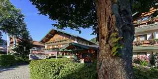 Traditionelles Hotelgebäude mit blumengeschmückten Balkonen und Garten vor blauem Himmel im Berchtesgadener Land
