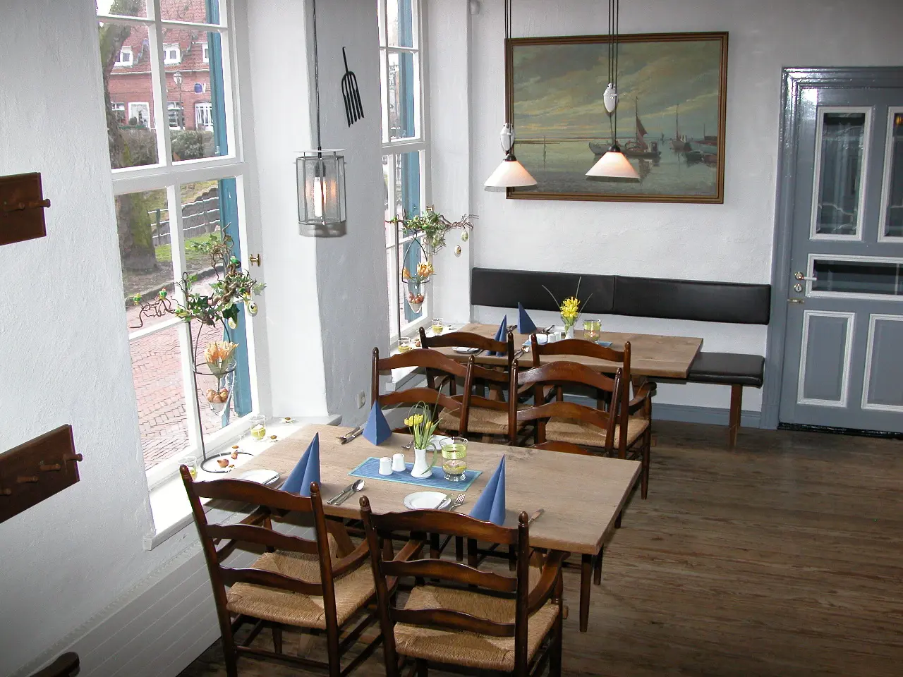 Restaurantbereich im Hohen Haus in Greetsiel mit Holztischen, blauen Servietten, Stühlen und maritim dekorierten Fenstern