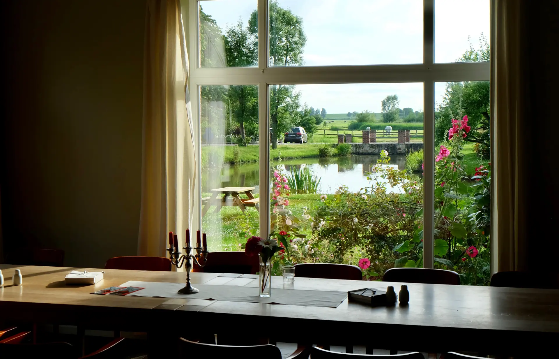 Hotel Kunze Hof Wattenmeer Jadebusen Außblick Großes Seminarzimmer mit Holztisch und Kerzenleuchter vor Fenster mit Blick auf Teich, Garten und grüne Landschaft im Seminarhotel Kunze-Hof Wattenmeer