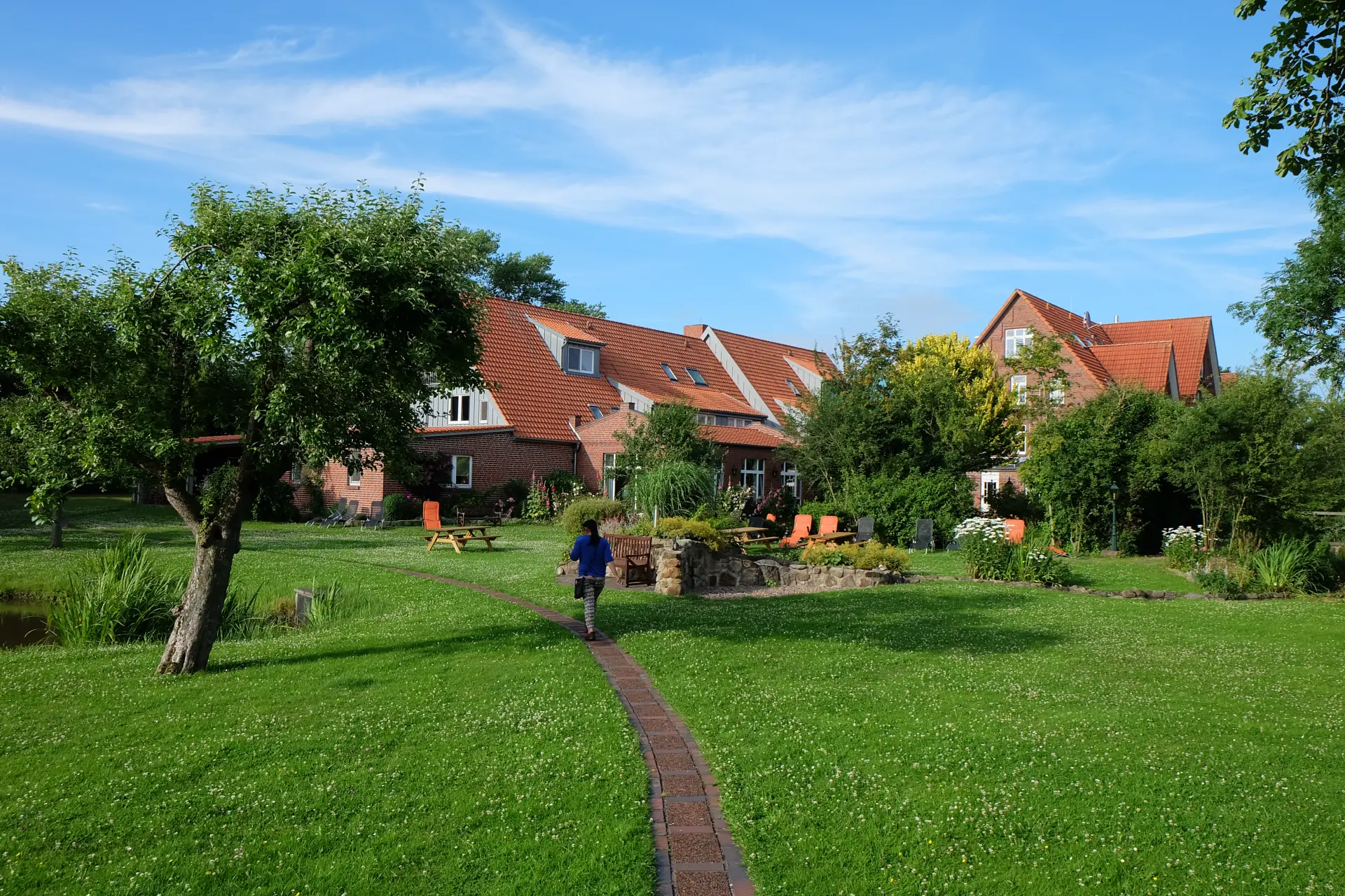 Hotel Kunze Hof Wattenmeer Jadebusen Weg Seminarhotel Kunze-Hof mit roten Dächern umgeben von grünem Garten und Wiesen, Spazierweg führt zur Unterkunft im Wattenmeer bei klarem Himmel
