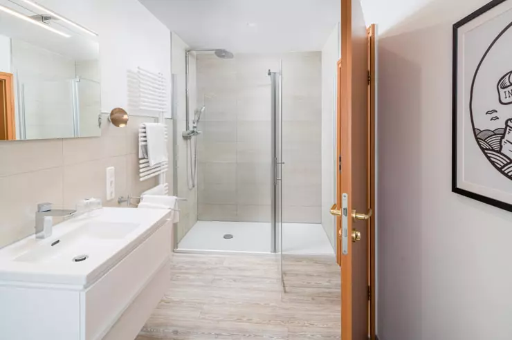 Hotel Inselfriede Spiekeroog Bad 40er Helles Badezimmer im Hotel Inselfriede Spiekeroog mit bodengleicher Dusche, weißem Waschtisch und Holztür