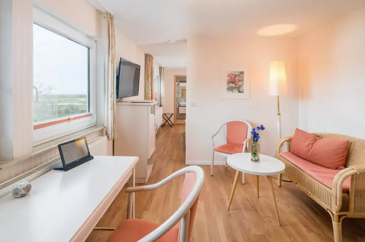 Hotel Inselfriede Spiekeroog Doppelzimmer 60 Hell eingerichteter Aufenthaltsraum im Hotel Inselfriede auf Spiekeroog mit Sitzbereich, Schreibtisch, TV und Fenster mit Blick nach draußen