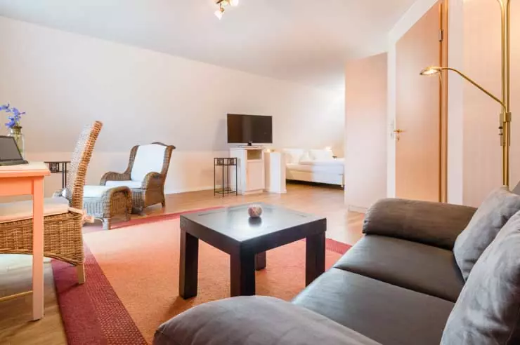 Hotel Inselfriede Spiekeroog Juniorsuite 61 Gemütlicher Wohnbereich mit Sofa, Sessel, Fernseher und Schreibtisch in einer modernen Hotelunterkunft auf Spiekeroog