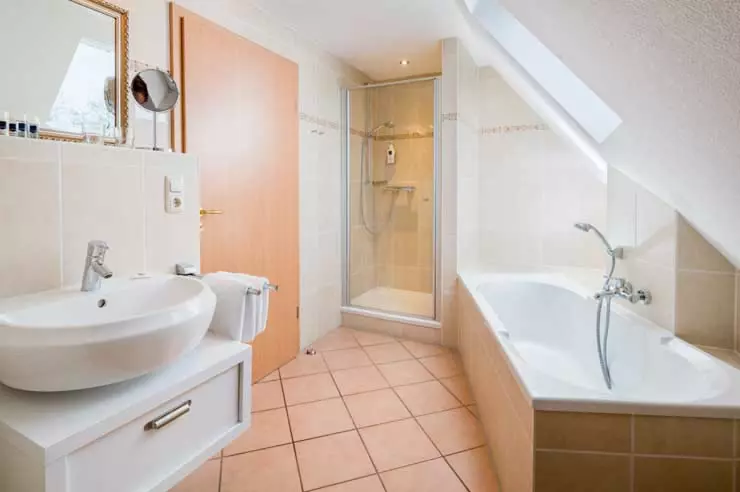 Hotel Inselfriede Spiekeroog Juniorsuite 61 Bad Helles Badezimmer im Hotel Inselfriede Spiekeroog mit Waschbecken, Dusche, Badewanne und Dachfenster unter Schräge