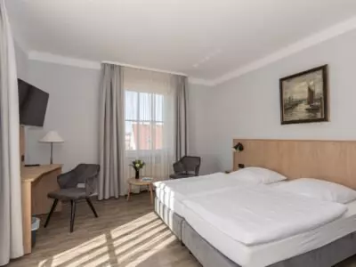 Helles Hotelzimmer mit zwei Einzelbetten, Sitzbereich, Schreibtisch, Fernseher und Fenster mit Blick auf Rügener Umgebung
