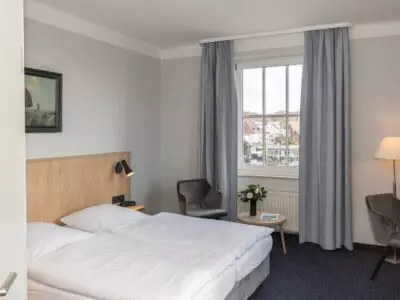 Modernes Hotelzimmer im Kurhotel Sassnitz auf Rügen mit Doppelbett, Sitzbereich, großem Fenster und neutraler, heller Einrichtung