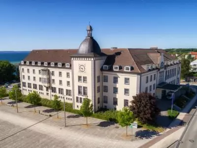 Kurhotel Sassnitz Aussenansicht Kurhotel Sassnitz mit Kuppel, Uhr und Parkplätzen, gelegen an der Küste von Rügen bei klarem Himmel