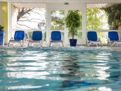 Innenbereich eines Schwimmbads im Kurhotel Sassnitz mit blauen Liegestühlen und großen Fenstern zum Garten auf Rügen