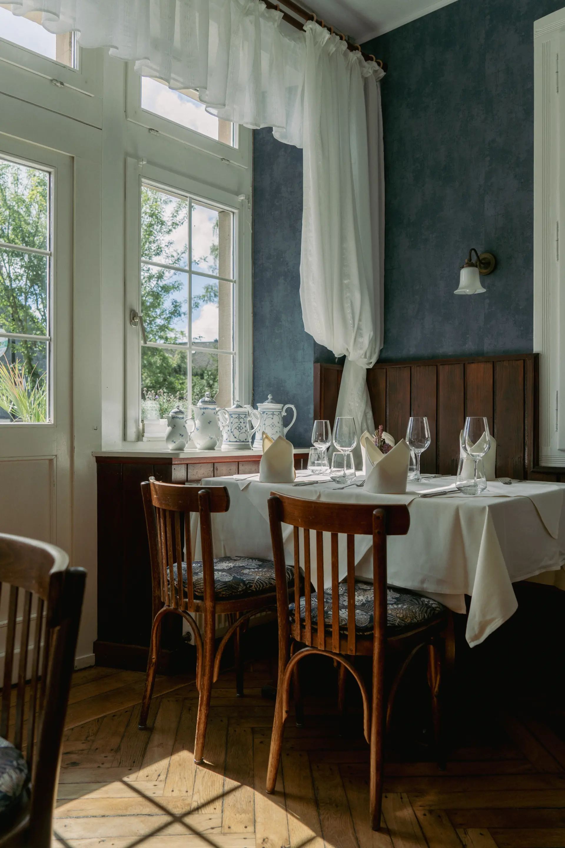 Eleganter gedeckter Tisch mit weißen Servietten, Gläsern und Holzmöbeln in einem hellen, rustikalen Zimmer im Landhaus Arnoth, Moselregion