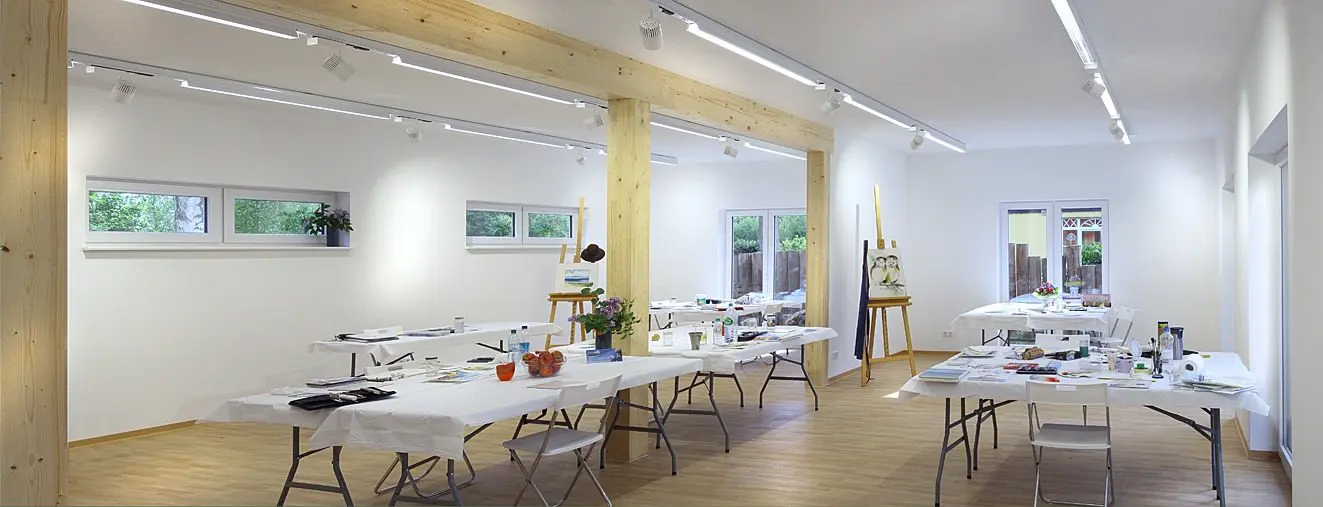 Offenes Atelier mit Tischen, Malutensilien und Staffelei im Künstlerhaus Prerow mit heller Innenraumgestaltung und Holzbalken