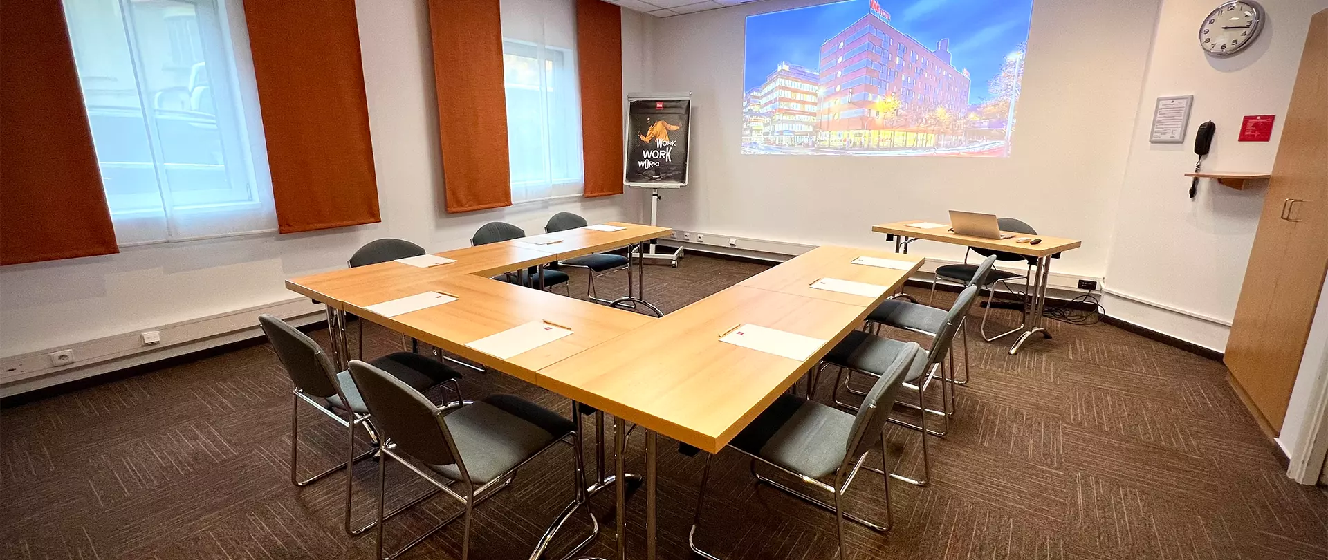 Moderner Konferenzraum mit U-förmigem Holztisch, Stühlen, Projektorbild und großen Fenstern im Atelier Ibis Praha Malá Strana in Prag