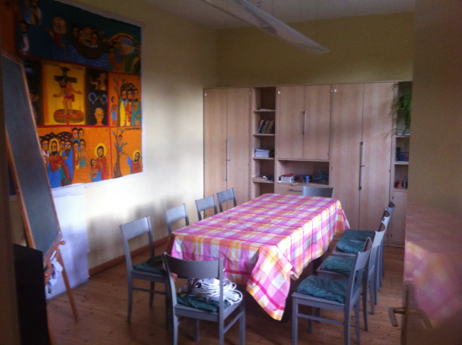 Prerow Gemeindehaus Konfirmandenraum Esszimmer mit bunt kariertem Tischtuch, acht Stühlen, großem Holzschrank und farbenfrohem Wandbild im Atelier Kantorhaus in Prerow