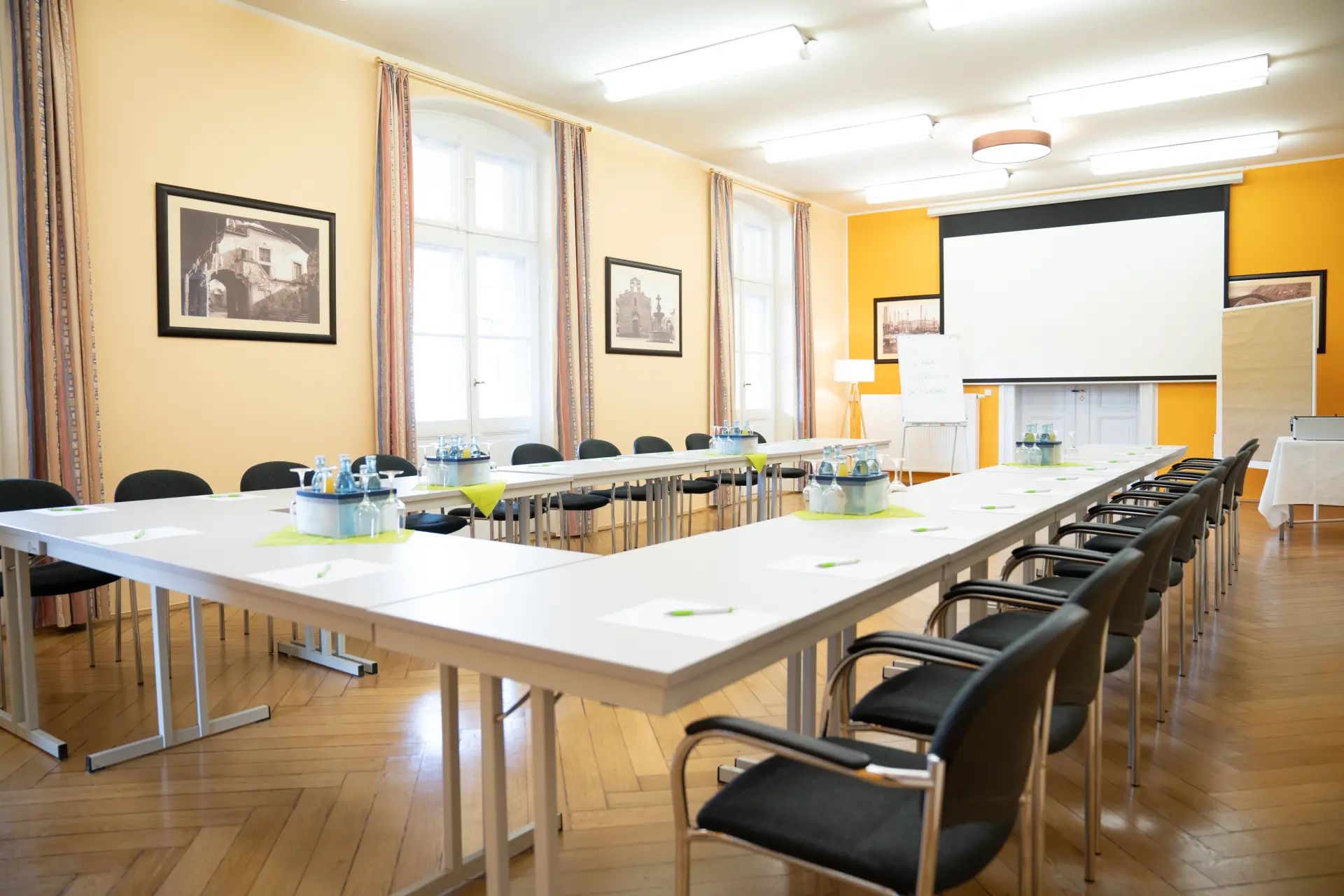 Konferenzraum im Atelier im Parkhotel Bad Schandau mit U-förmigen Tischen, schwarzen Stühlen, Wasserflaschen und Leinwand in der Sächsischen Schweiz
