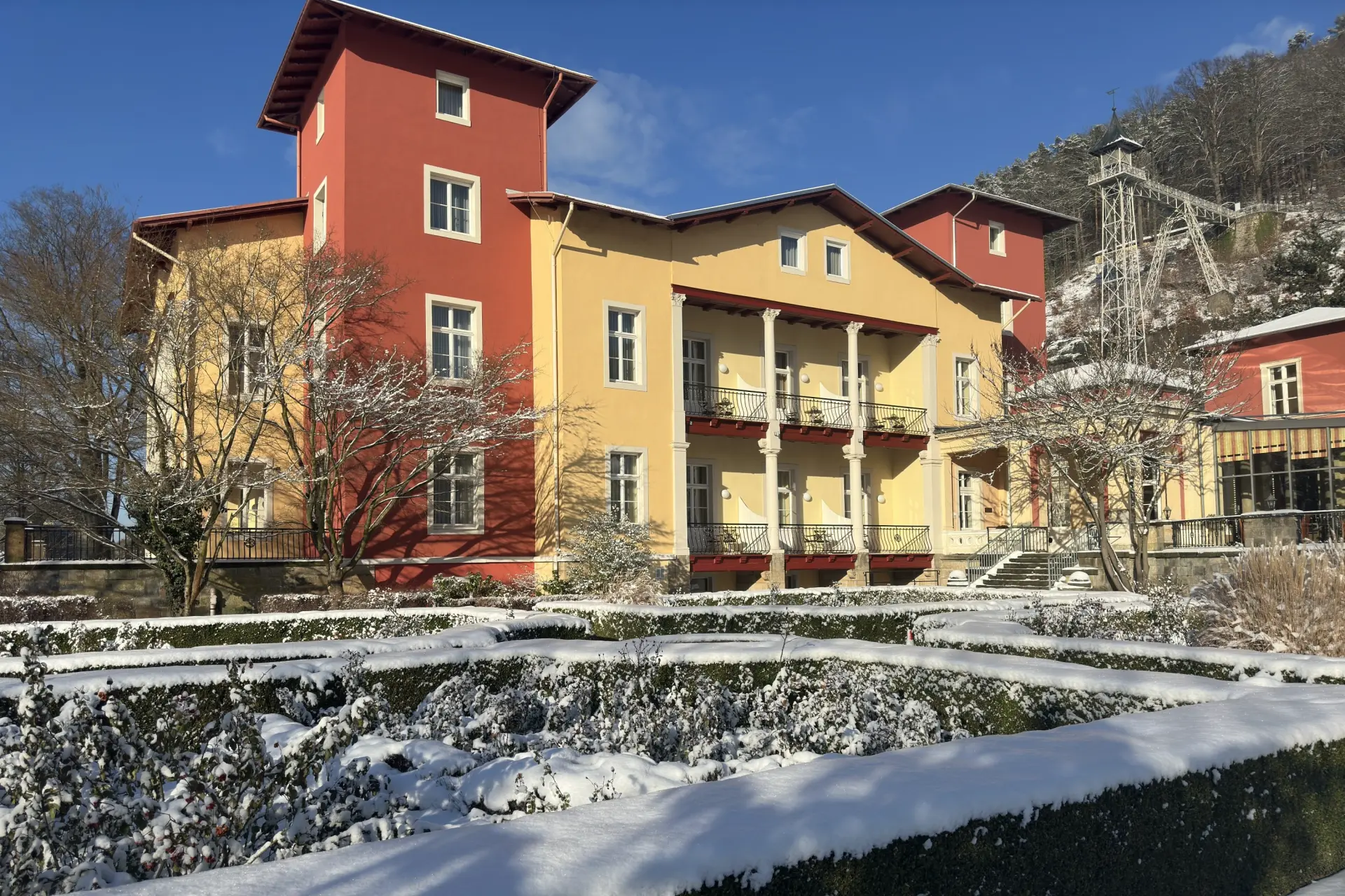 Gelbes und rotes Parkhotel Bad Schandau in winterlicher Landschaft mit schneebedeckten Bäumen und Garten in der Sächsischen Schweiz